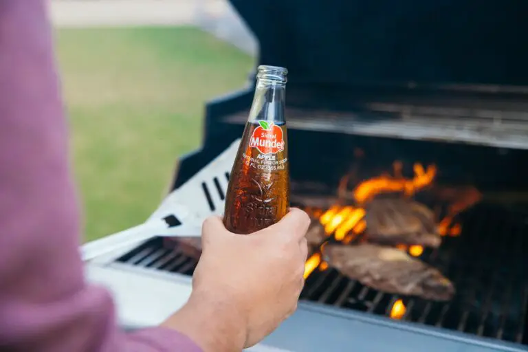 a person holding a bottle of beer near a grill